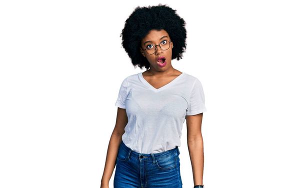 Молодая африканская американка в белой футболке с шокирующим лицом, выглядит скептически и саркастично, удивлена с открытым ртом  - Фото, изображение
