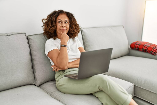Középkorú spanyol nő dolgozik számítógép laptop otthon komoly arc gondolkodás kérdés kézzel az állon, átgondolt zavaró ötlet  - Fotó, kép