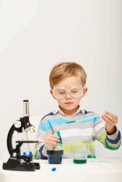 Een jongen van vijf die experimenteert met gekleurde vloeistoffen. Chemische experimenten van een kleine wetenschapper jongen van Europees uiterlijk. - Foto, afbeelding
