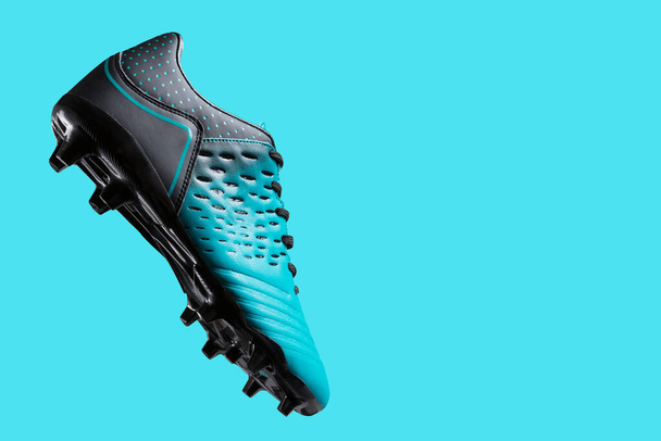 футбольные ботинки висят в воздухе, как будто бьют по мячу, концепция, спортивная обувь для футбола, на бирюзовом фоне - Фото, изображение