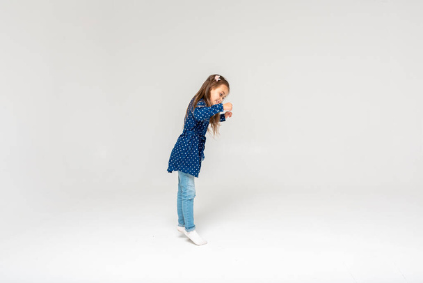 Foto de tamaño completo de una chica saltando y levantando puños en una camisa azul y jeans, aislado sobre un fondo blanco, enfoque selectivo, movimiento - Foto, Imagen