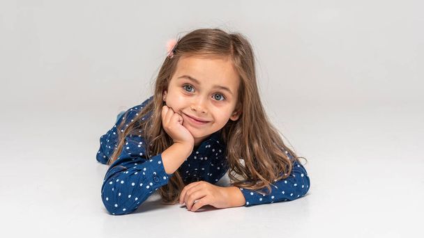 Beautiful little girl lying on the floor smiling, and propped his head with his hand on a white background. The concept of a happy childhood, well-being in the family. isolated - Foto, Bild