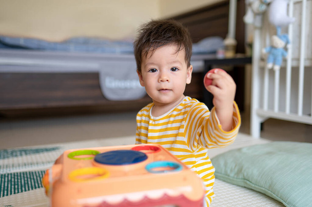 8 months old mixed race baby boy playing with activity box in the bedroom wearing yellow pajama while sitting on the floor covered with a rubber play mat - Fotó, kép