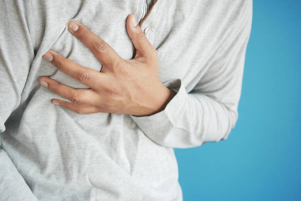jonge man lijden pijn in het hart en houden borst met de hand  - Foto, afbeelding