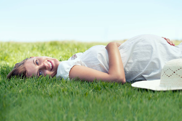 Shes counting down the days. A pretty woman lying on the grass outdoors and relaxing in the sunshine. - Photo, Image