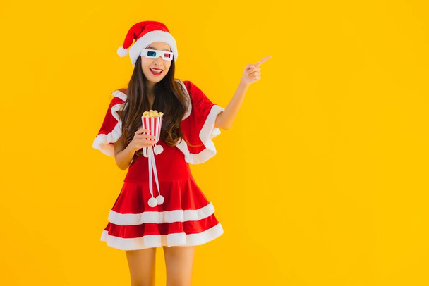 Portrait beautiful young asian woman wear christmas clothes hat with popcorn and 3d glasses ready for watch movie on yellow isolated background - Photo, Image