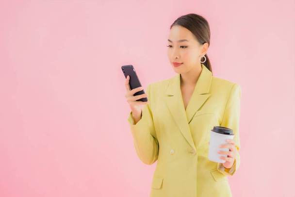 Портрет красивая молодая азиатская деловая женщина использовать смартфон с чашкой кофе на цветном фоне - Фото, изображение