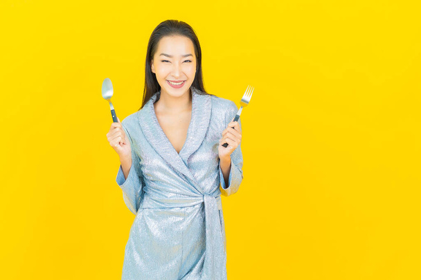 Portret mooie jonge aziatische vrouw glimlach met lepel en vork op gele kleur achtergrond - Foto, afbeelding