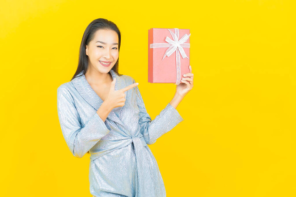 Portrait beautiful young asian woman smile with red gift box on yellow color background - Φωτογραφία, εικόνα