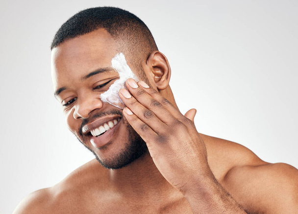 Using a moisturiser ensures that the skins blemishes are camouflaged. Studio shot of a handsome young man applying moisturiser to his face against a white background. - Photo, Image