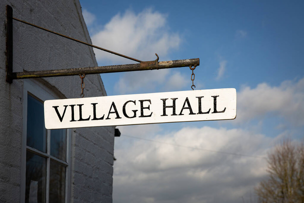Un letrero del Village Hall colgado de un edificio comunitario local que es un lugar de encuentro para los residentes de un pequeño barrio inglés - Foto, Imagen