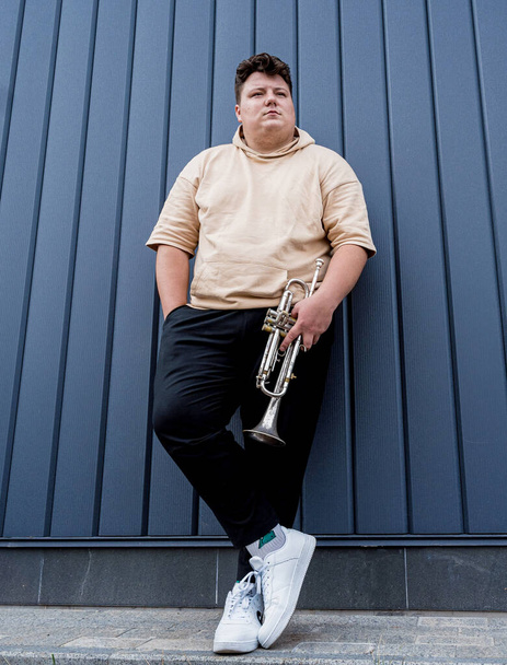 Young street musician playing the trumpet near the big blue wall - Zdjęcie, obraz