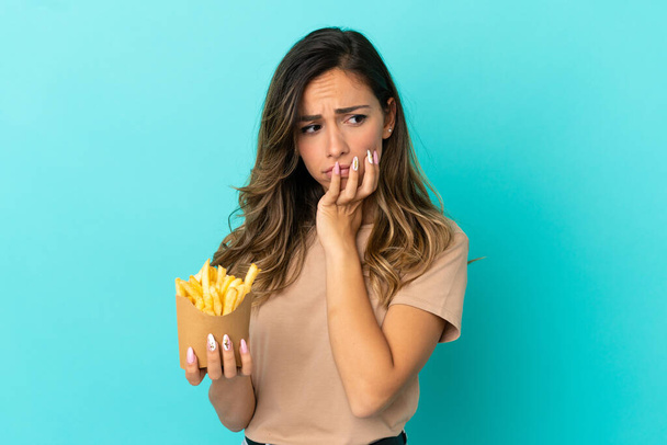 Junge Frau mit Pommes frites vor isoliertem Hintergrund hat Zweifel - Foto, Bild