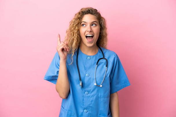 Νεαρή χειρουργός γιατρός γυναίκα απομονωμένη σε ροζ φόντο σκέφτεται μια ιδέα δείχνοντας το δάχτυλο προς τα πάνω - Φωτογραφία, εικόνα