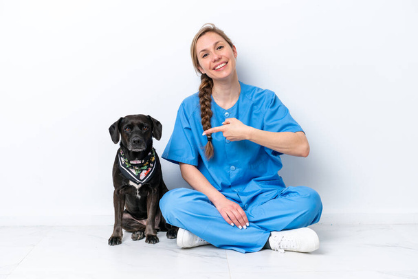 Giovane donna veterinario con cane seduto sul pavimento isolato su sfondo bianco e che lo indica - Foto, immagini