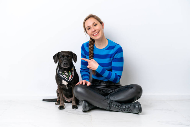 Young caucasian woman sitting on the floor with his puppy isolated on white background and pointing it - Photo, Image