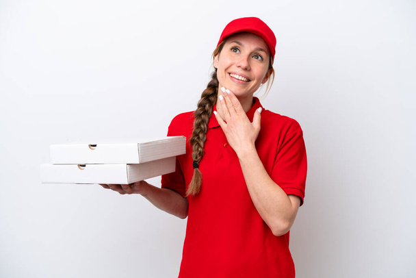 Mujer de entrega de pizza con uniforme de trabajo recogiendo cajas de pizza aisladas sobre fondo blanco mirando hacia arriba mientras sonríe - Foto, Imagen