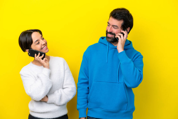 Joven pareja caucásica aislada sobre fondo amarillo hablando con móvil - Foto, Imagen