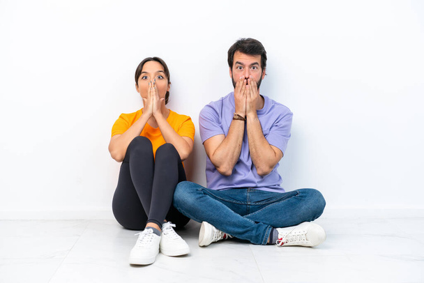 Young caucasian couple sitting on the floor isolated on white background with surprise facial expression - Fotografie, Obrázek