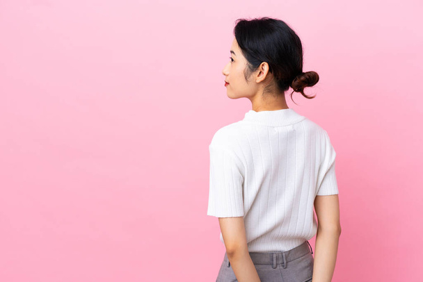 Young Vietnamese woman isolated on pink background in back position and looking back - Photo, Image