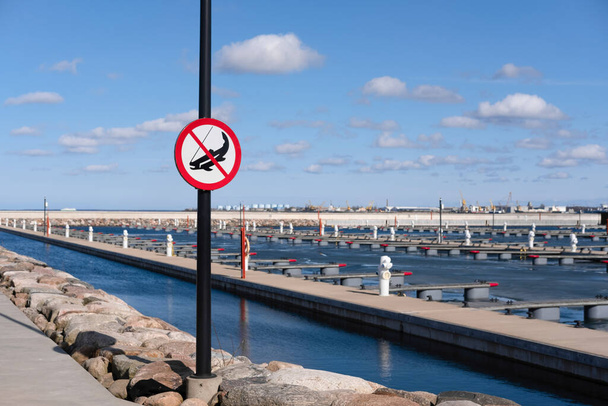 Fishing is prohibited in modern yacht port. No fishing sign against blue sky on pier with boat docks and sea on the background. Summer activities on vacation. Close up, copy space - Photo, image
