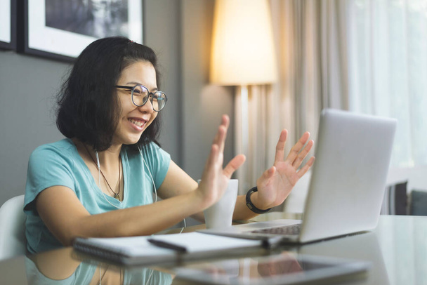 Attractive smiling young Asian woman waving hands on a video call, Young female studying on laptop computer. - 写真・画像