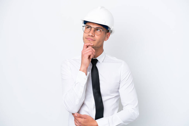 Young architect caucasian man with helmet and holding blueprints isolated on white background and looking up - Foto, imagen