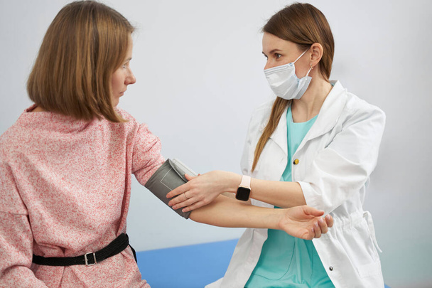 Doctor checking woman blood pressure in clinic - Fotó, kép