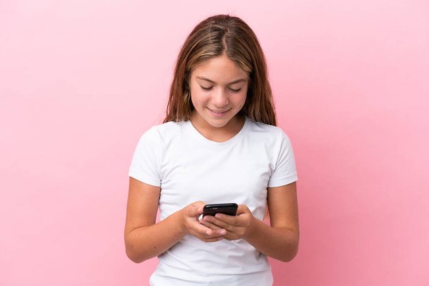 Little caucasian girl isolated on pink background sending a message with the mobile - Фото, изображение