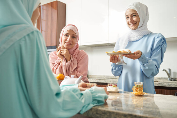 Freundliche Muslimin bietet leckeres Gebäck an und lächelt - Foto, Bild
