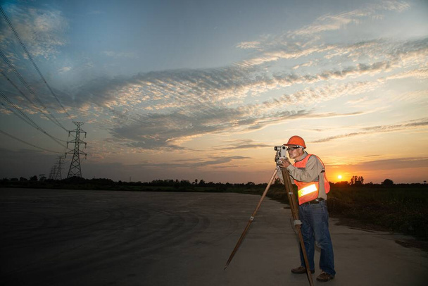Engineer or surveyor working with theodolite equipment at a field have high voltage in background on sunset time. - Zdjęcie, obraz