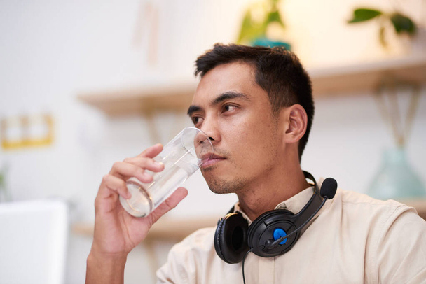 A sick Asian man drinks an effervescent flu tablet in water at work at his desk - Foto, Imagen