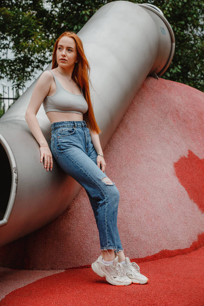 Stylish beautiful woman model in hipster jeans. Outdoor fashion portrait of glamour sensual young girl,wear cool outfit, red hair. Side view full length beautiful girl relax enjoy sunshine. - Foto, Imagem