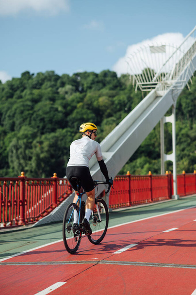Чоловічий велосипедист у вбранні їде на велосипедній доріжці на мосту, вид ззаду. Вертикальний
 - Фото, зображення
