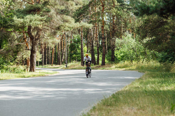 A professional cyclist man rides a bicycle outside the city on an asphalt road in the woods. - Photo, Image