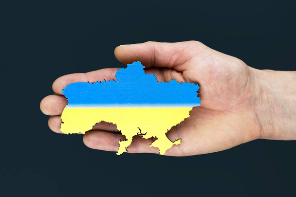 Männliche Hände halten eine Landkarte der Ukraine auf schwarzem Hintergrund. Ukrainisch blau-gelbe Flagge. Konzept - Foto, Bild