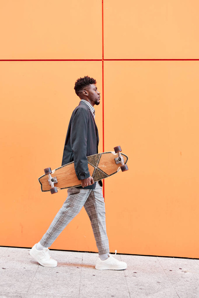 joven con chaqueta y monopatín caminando por la calle sobre un fondo naranja. - Foto, Imagen