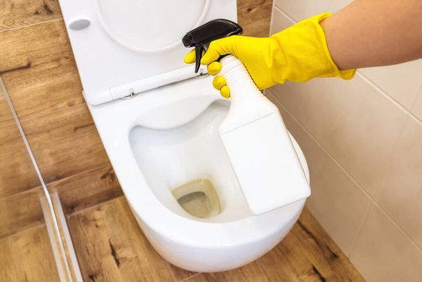 Κοντινό πλάνο των χεριών σε γάντια χρησιμοποιώντας καθαριστικό διάλυμα για την απολύμανση της τουαλέτας, μπουκάλι mockup - Φωτογραφία, εικόνα
