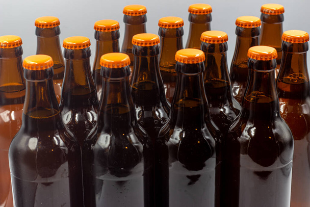 Vereinzelte hausgemachte Biere ohne Etiketten, mit weißem Hintergrund. Nahaufnahme der Bierflaschen mit orangefarbenen Verschlüssen. Vereinzelte Bierflaschen mit orangefarbenen Verschlüssen.  - Foto, Bild