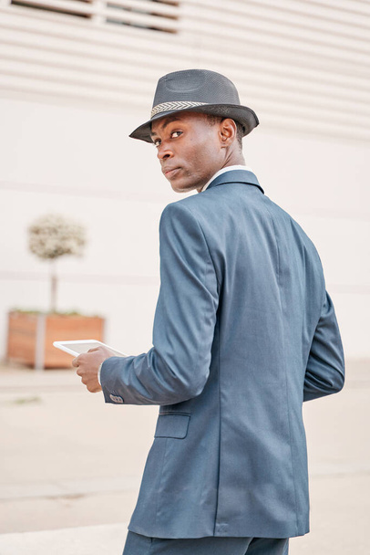 businessman in suit and hat using a table pc. back view of a young african american man looking to the side. - Foto, afbeelding
