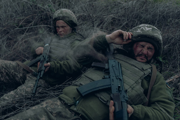 2人のウクライナ兵は、ロシアの敵による砲撃の間、乾いた草の上にカラシニコフのアサルトライフルで横たわっている。ウクライナにおけるロシアの軍事侵攻の概念。ウクライナとヨーロッパでの戦争. - 写真・画像