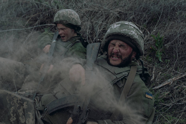 2人のウクライナ兵は、ロシアの敵による砲撃の間、乾いた草の上にカラシニコフのアサルトライフルで横たわっている。ウクライナにおけるロシアの軍事侵攻の概念。ウクライナとヨーロッパでの戦争. - 写真・画像