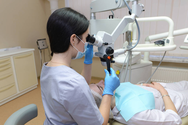 Estomatólogo examinando los dientes del paciente con la ayuda de un microscopio dental profesional. Dentista prevenir la caries utilizando instrumentos de restauración. Cliente acostado en silla de dentista
. - Foto, imagen