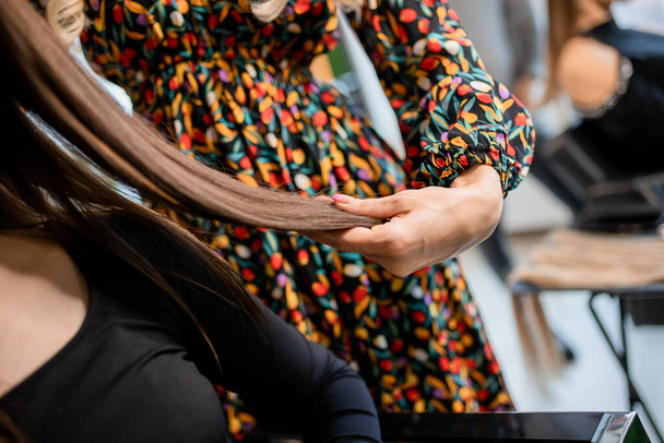 A professional hairdresser prepares brunette hair for extensions in a beauty salon while trying it on for a client - Foto, afbeelding
