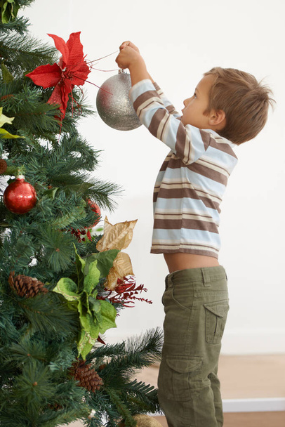 Hes decorating the tree on his own this year. Shot of a young boy decorating a christmas tree by himself. - Foto, immagini