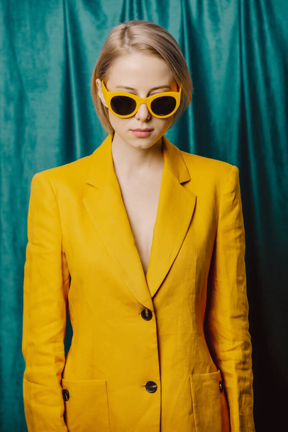 Stylish ukrainian woman in yellow sunglasses and jacket on green curtains background - Фото, изображение