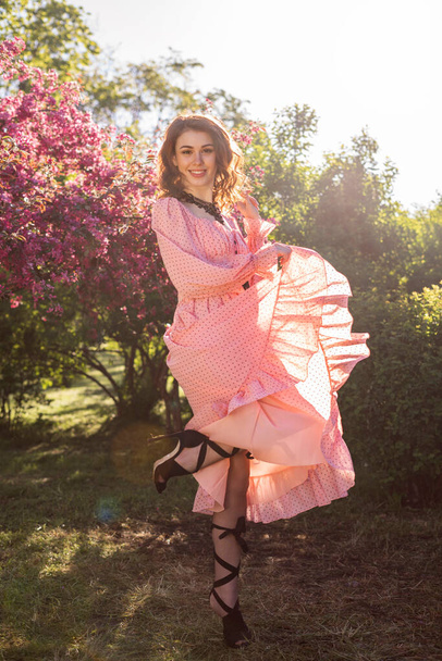 Retrato de uma menina feliz bonita nova com cabelo marrom longo em um vestido rosa em um fundo de flores de cereja. - Foto, Imagem