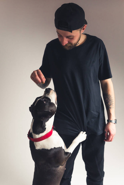 Vertical studio shot of a dog owner guy in black clothes giving dog treats to his animal best friend. - Fotografie, Obrázek