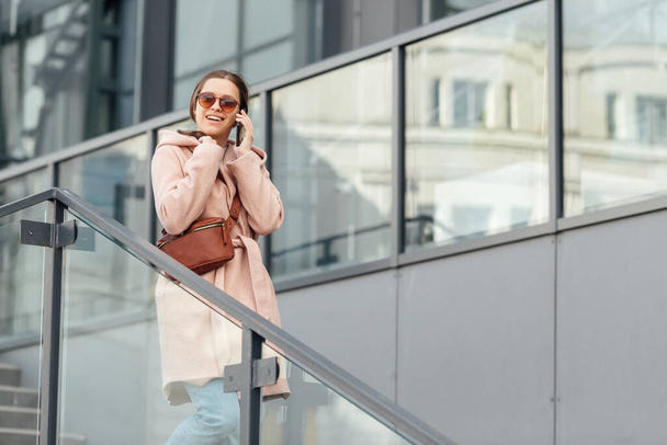 Woman in pink dress talking to smarthone outdoor on grey urban city background - Fotoğraf, Görsel
