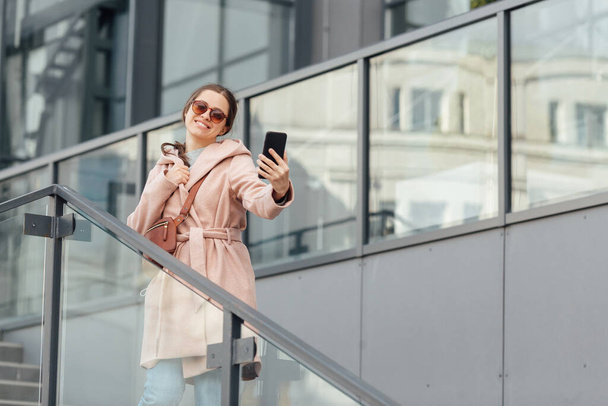 Woman in pink dress take selfie on smarthone on grey urban background outdoor - Foto, Imagem